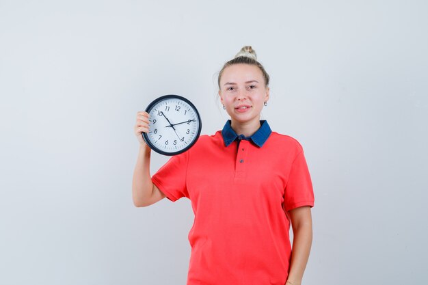 Jonge vrouw met klok in t-shirt en op zoek vrolijk