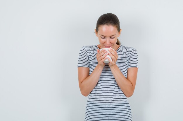 Jonge vrouw met kopje thee en glimlachend in t-shirt vooraanzicht.