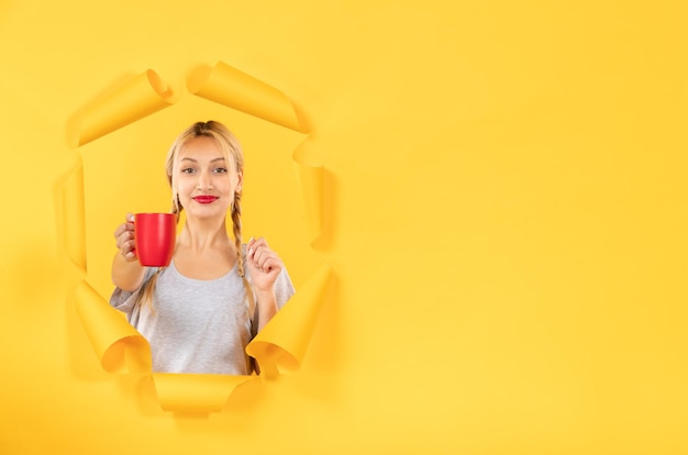 Jonge vrouw met kopje thee op gescheurd geel papier oppervlak winkelen reclame gezichtsbehandeling