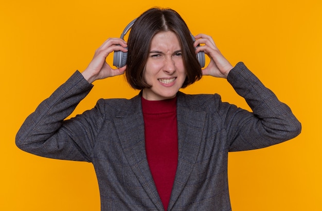 Jonge vrouw met kort haar grijze jas met koptelefoon dragen