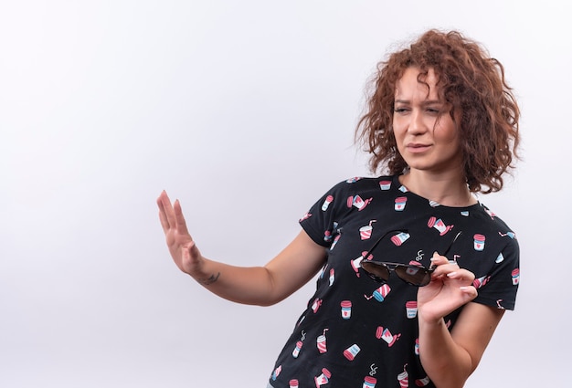 Jonge vrouw met kort krullend haar die haar armen uitstrekt en een verdedigingsgebaar maakt als tellin komt niet dichterbij over een witte muur