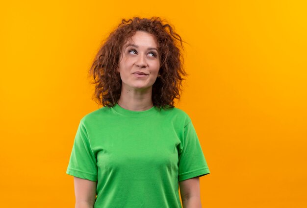 Jonge vrouw met kort krullend haar in groen t-shirt opzoeken met dromerige blik staan