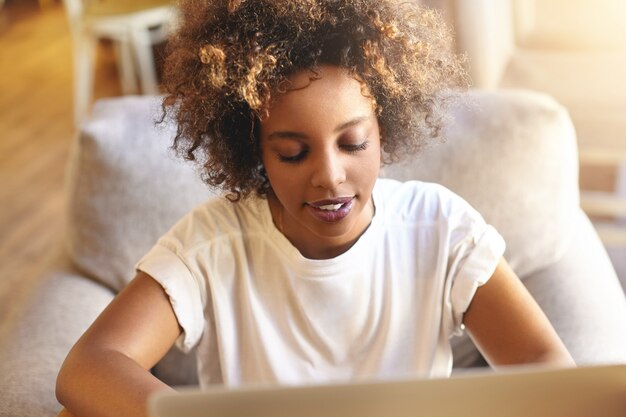 Gratis foto jonge vrouw met krullend haar die laptop met behulp van