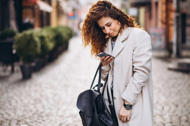 Jonge vrouw met krullend haar die telefoon met behulp van bij de straat