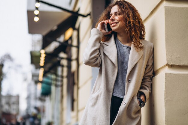 Jonge vrouw met krullend haar die telefoon met behulp van bij de straat