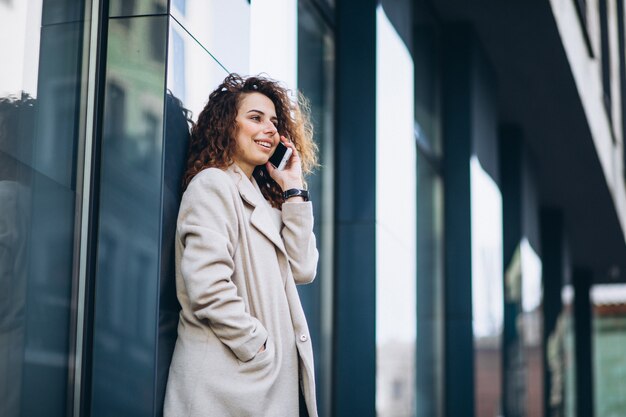 Jonge vrouw met krullend haar die telefoon met behulp van bij de straat