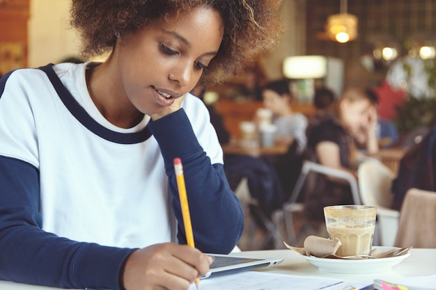 Jonge vrouw met krullend haar met behulp van tablet in café