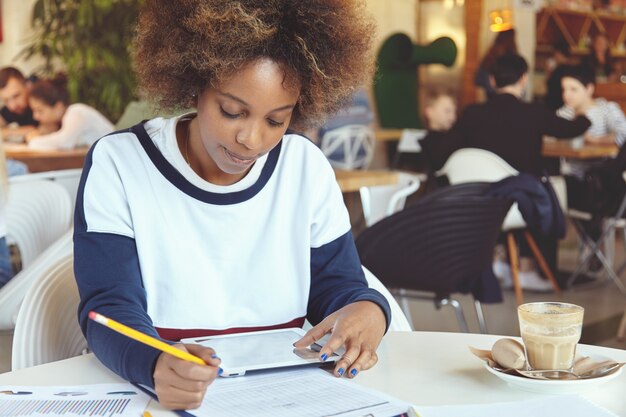 Jonge vrouw met krullend haar met behulp van tablet in café