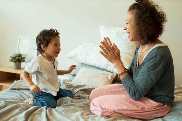 Jonge vrouw met krullend haar, zittend op bed met schattige zoon