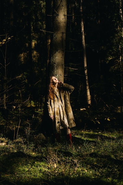 Jonge vrouw met lang rood haar in een linnenkleding die paddestoelen in het bos verzamelen