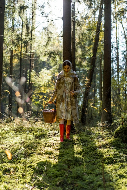 Jonge vrouw met lang rood haar in een linnenkleding die paddestoelen in het bos verzamelen