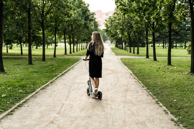 Jonge vrouw met lange haren op elektrische autoped. Het meisje op de elektrische scooter.