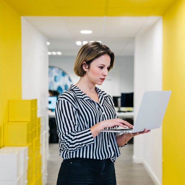 Jonge vrouw met laptop in de hal van kantoor