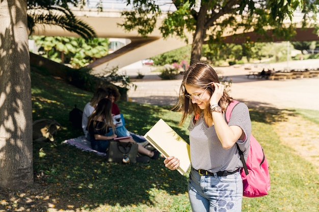 Jonge vrouw met leerboek en rugzak in park