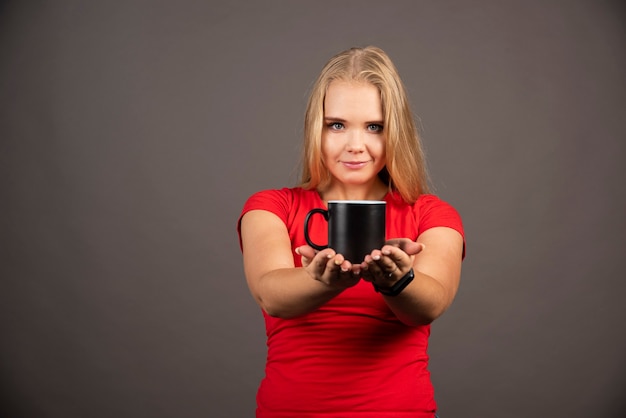 Jonge vrouw met lege beker op zwarte muur.