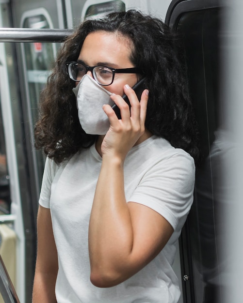 Jonge vrouw met medisch masker praten aan de telefoon in de metro