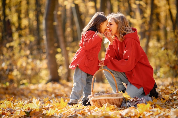 Jonge vrouw met meisje wandelen in herfst bos. blonde vrouw speelt met haar dochter. moeder en dochter dragen jeans en rode jassen. Premium Foto