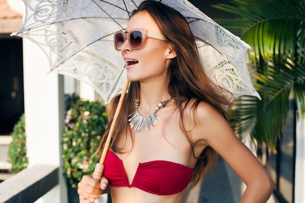 Jonge vrouw met mooi slank lichaam dragen rode bikini badpak kant parasol houden op tropische villa resort tijdens vakantie reizen in Azië, mager figuur, zomer stijl trend accessoires