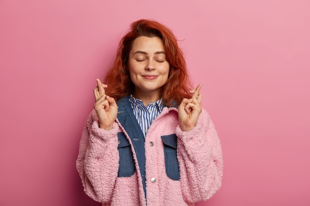 Jonge vrouw met natuurlijk golvend rood haar ondersteunt vrienden, wenst veel geluk, kruist de vingers en wacht op een mooi resultaat