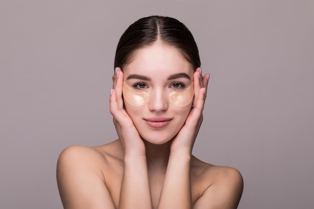 Jonge vrouw met oogvlekken wat betreft tempels die op grijze muur worden geïsoleerd. cosmetica, huidstress concept