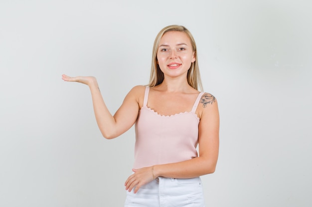 Jonge vrouw met open handpalm in singlet, minirok en op zoek vrolijk.