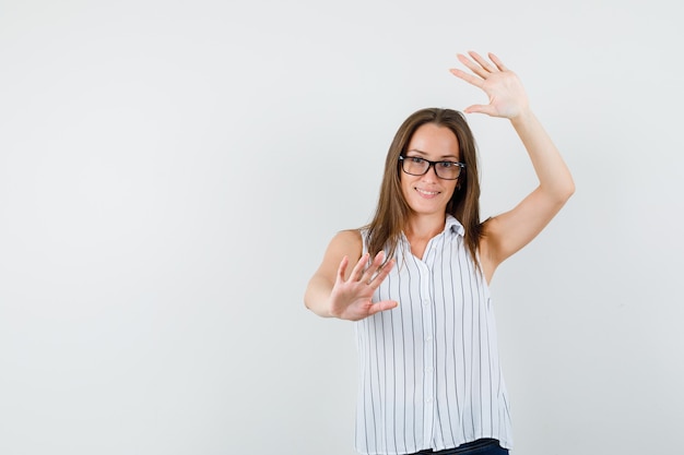 Jonge vrouw met opgeheven handpalmen in t-shirt, spijkerbroek en op zoek grappig, vooraanzicht.