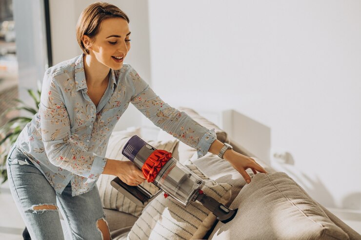 Gratis Foto jonge vrouw met oplaadbare stofzuiger die thuis schoonmaakt