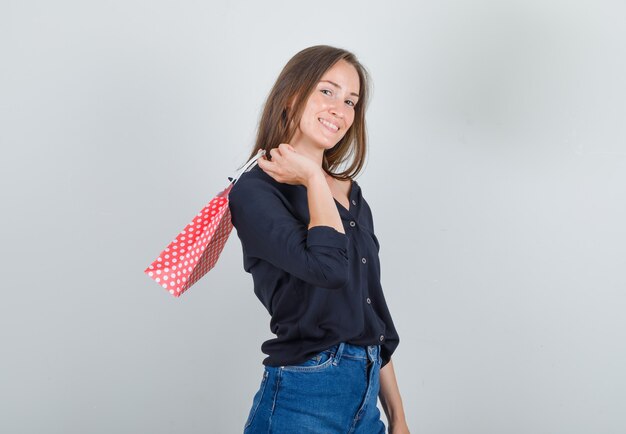 Jonge vrouw met papieren zak in zwart shirt, jeans broek en op zoek vrolijk