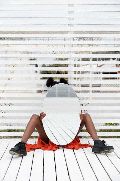 Gratis foto jonge vrouw met rode jurk poseren buiten met spiegel