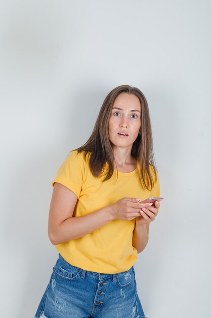 Jonge vrouw met smartphone in t-shirt, korte broek en op zoek verward