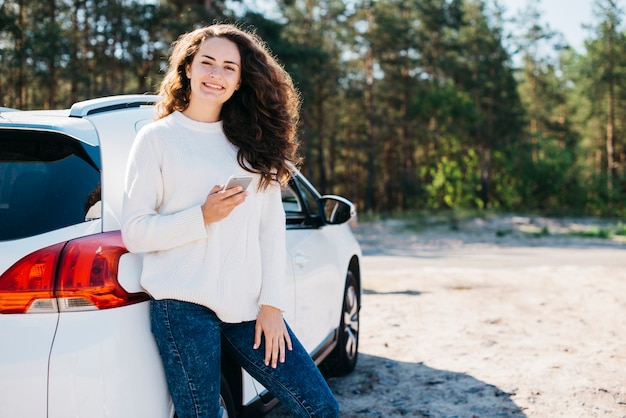 Jonge vrouw met smartphone naast haar auto