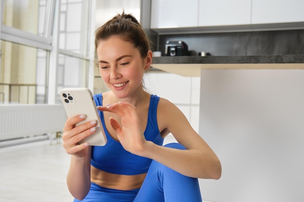 Gratis foto jonge vrouw met smartphone traint thuis met behulp van de mobiele telefoon-app voor sporttraining binnenshuis