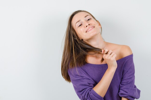 Jonge vrouw met streng terwijl poseren in violet overhemd en vrolijk kijken. vooraanzicht.