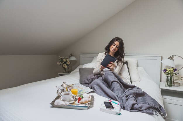 Jonge vrouw met tablet zittend op het bed