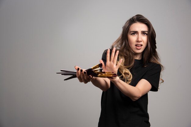 Jonge vrouw met verfborstels op grijze muur.