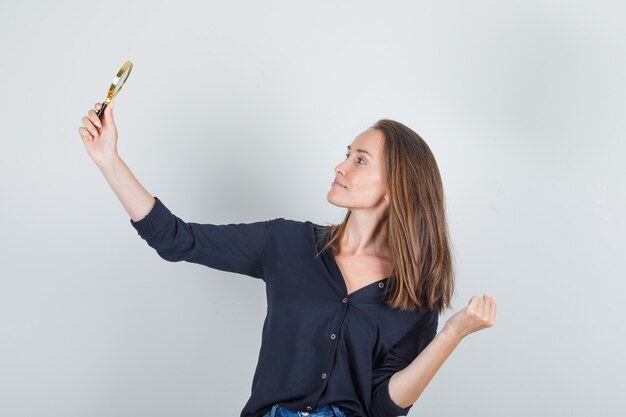 Jonge vrouw met vergrootglas zoals het nemen van selfie in zwart shirt