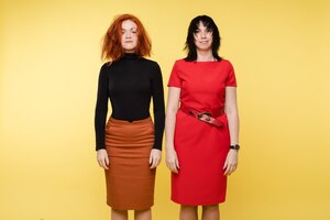 Jonge vrouw met verwarde haren poseren na conflict geïsoleerd op gele studio achtergrond. twee mode-vriendinnen of stijlvolle zakenvrouwen met positieve emotie
