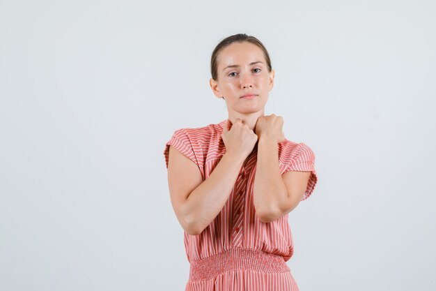 Jonge vrouw met vuisten op de kraag in gestreepte jurk, vooraanzicht.