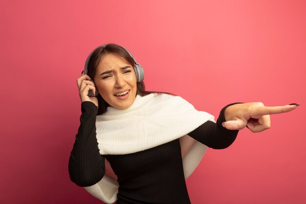 Jonge vrouw met witte sjaal en hoofdtelefoons die met indexfigner naar iets gelukkig en vrolijks wijzen