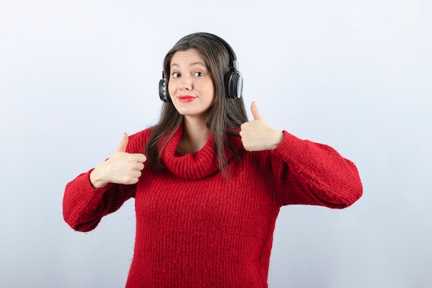 Jonge vrouw model in rode trui met koptelefoon duimen opdagen