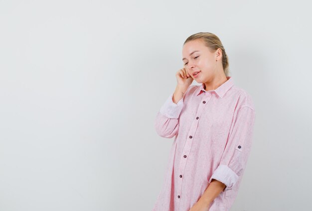 Jonge vrouw naar beneden te kijken terwijl ze in roze shirt denkt en hoopvol kijkt