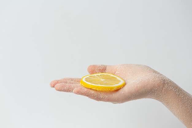 Jonge vrouw natuurlijke citroen scrub toe te passen op handen tegen wit oppervlak
