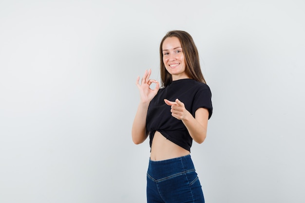 Jonge vrouw ok teken tonen, wijzend op camera in zwarte blouse