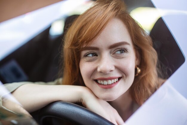 Jonge vrouw omarmen haar nieuwe auto Opgewonden jonge vrouw en haar nieuwe auto binnenshuis Jonge en vrolijke vrouw genieten van nieuwe auto knuffelen stuurwiel zitten binnen