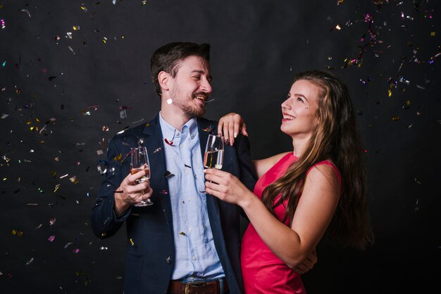 Jonge vrouw omhelst de mens met glazen drank tussen het werpen van confettien