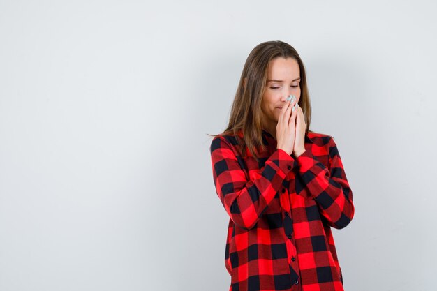 Jonge vrouw omklemde handen in biddende positie in geruit hemd en zag er hoopvol uit, vooraanzicht.