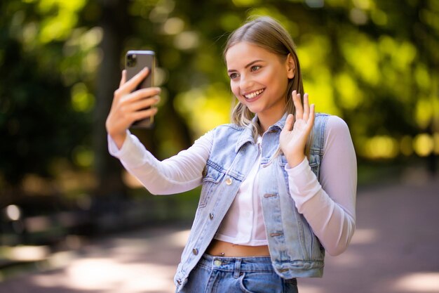 Jonge vrouw online chatten op een mobiele telefoon terwijl ze op een zonnige dag in een park zit en videogesprek heeft met een vriend buiten in de vrije tijd