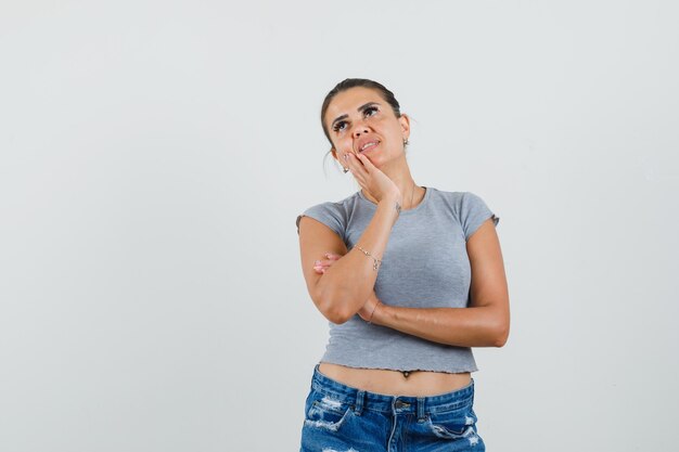 Jonge vrouw op zoek naar boven in t-shirt, korte broek en peinzend op zoek