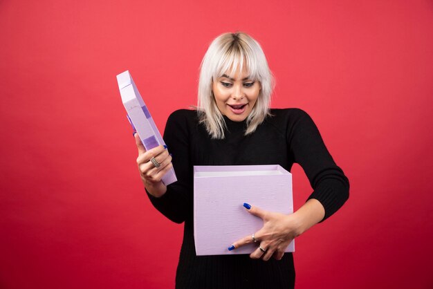 Jonge vrouw opgewonden over een cadeautje op een rode muur.