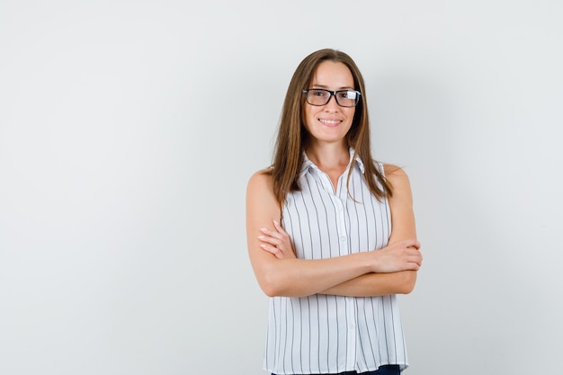 Jonge vrouw permanent met gekruiste armen in t-shirt, spijkerbroek en op zoek vrolijk, vooraanzicht.